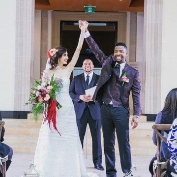 Newlyweds raising their joined hands as Wayde celebrates behind them