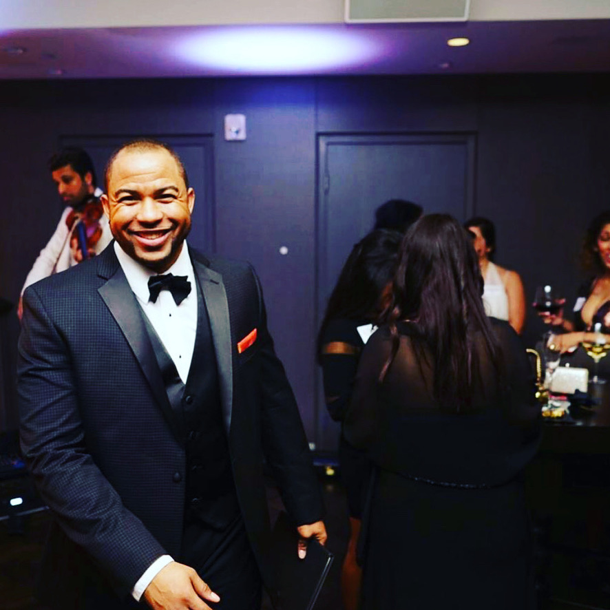 Wayde smiling in a tuxedo at a wedding reception