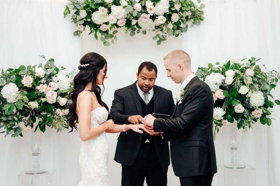 Wayde guiding a ring exchange beneath abundant white florals