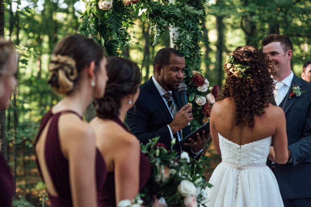Wayde speaking to a couple beneath a woodland floral arbor